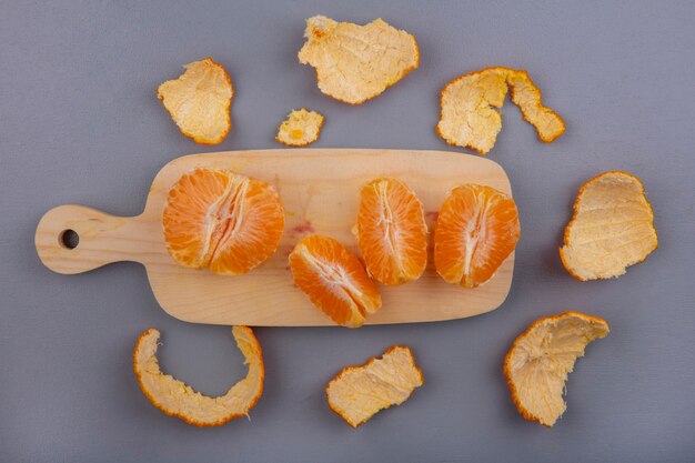 Vista superior de naranjas peladas en tabla de cortar con cáscara sobre fondo gris
