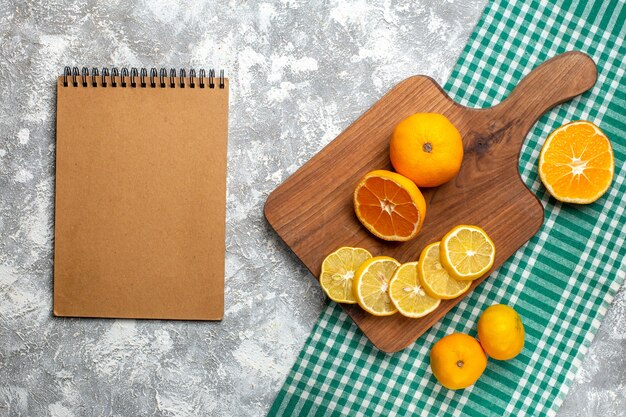 Vista superior naranjas rodajas de limón en limones de tablero de madera en el bloc de notas de mantel a cuadros blanco verde sobre mesa gris