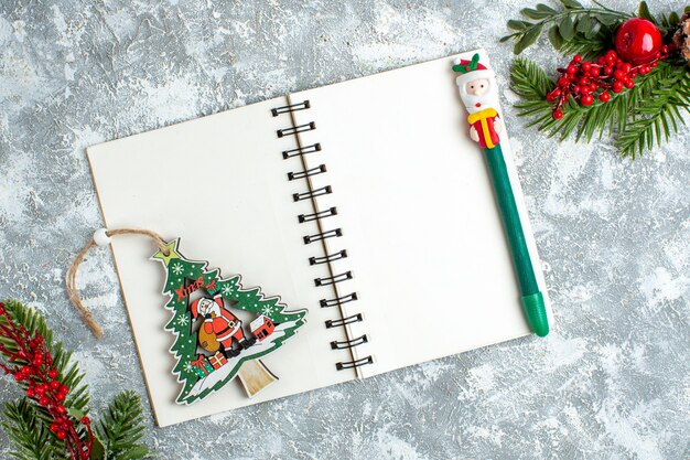 Vista superior de Navidad adorno de árbol de Navidad de bayas rojas y lápiz en el bloc de notas en la mesa blanca gris