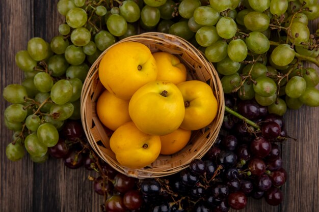 Vista superior de nectacots en canasta y uvas alrededor sobre fondo de madera