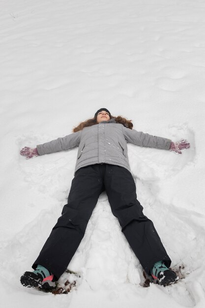 Vista superior de una niña jugando en la nieve con ropa de abrigo