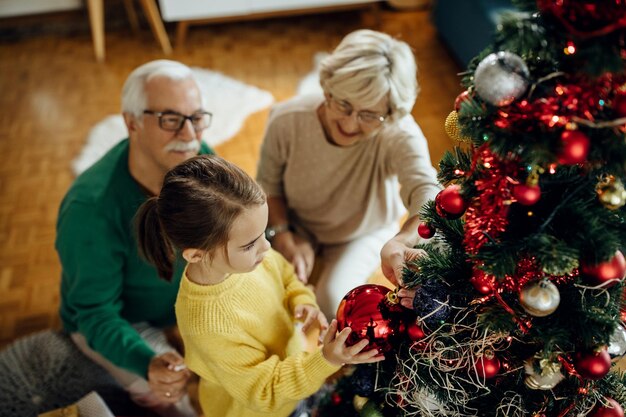 Vista superior de una niña pequeña decorando el árbol de Navidad con sus abuelos