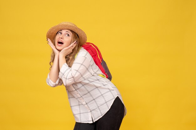Vista superior de la niña viajera sonriente con su sombrero y mochila roja posando para la cámara en amarillo