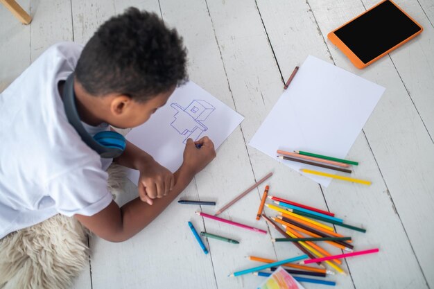 Vista superior del niño dibujante tirado en el suelo