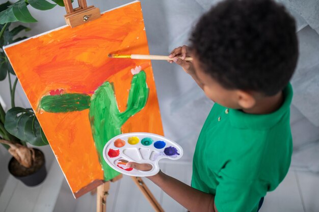 Vista superior del niño con pintura de paleta en caballete