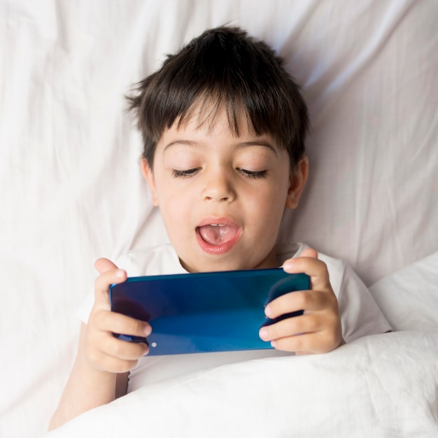 Vista superior de niño con teléfono en la cama