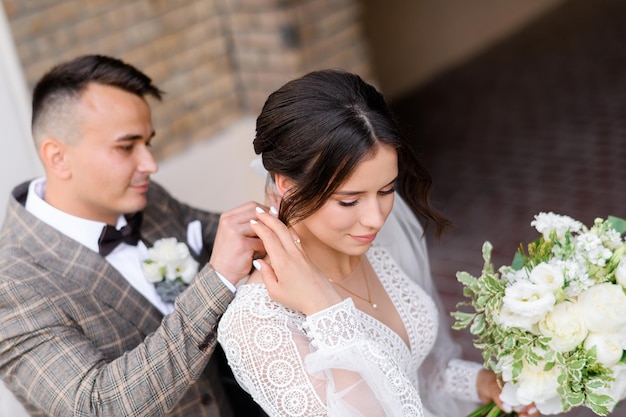 Vista superior del novio pensativo en traje de moda haciendo un regalo de boda para la novia y atando joyas en su cuello Mujer atractiva