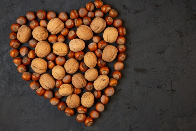 Vista superior de nueces y avellanas enteras dispuestas en forma de corazón en la oscuridad