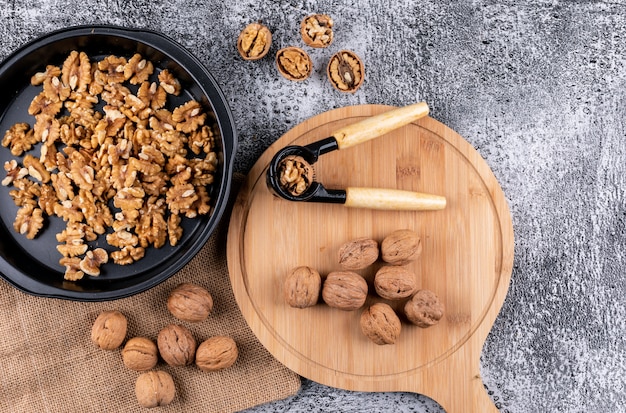 Vista superior de nueces con cascanueces en tabla de cortar de madera y sartén negro