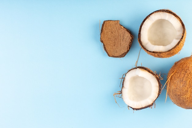 Una vista superior de nueces de coco en rodajas y todo dulce lechoso fresco aislado en el azul hielo