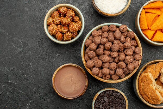 Vista superior de nueces dulces con copos de cacao y cips en el color oscuro del desayuno de la comida de la leche del bocadillo del escritorio