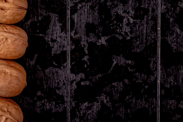 Vista superior de nueces enteras alineadas en una fila sobre fondo de madera negra con espacio de copia