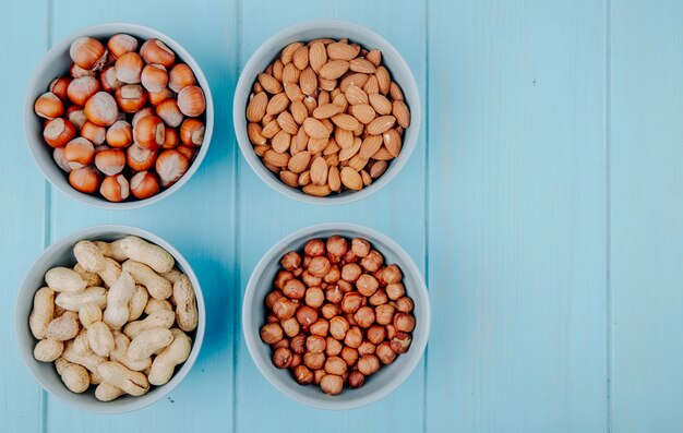 Vista superior de nueces mixtas con cáscara y sin cáscara en cuencos avellanas y cacahuetes sobre fondo azul con espacio de copia