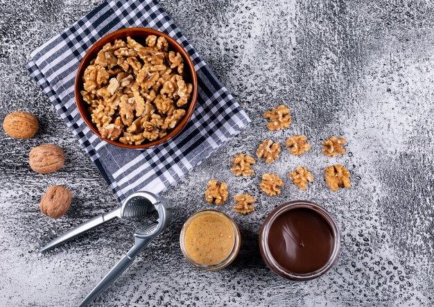 Vista superior de nueces en un tazón, cascanueces y nueces mantequilla en madera horizontal