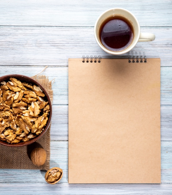 Vista superior de nueces en un tazón cuaderno de bocetos y una taza con té en madera