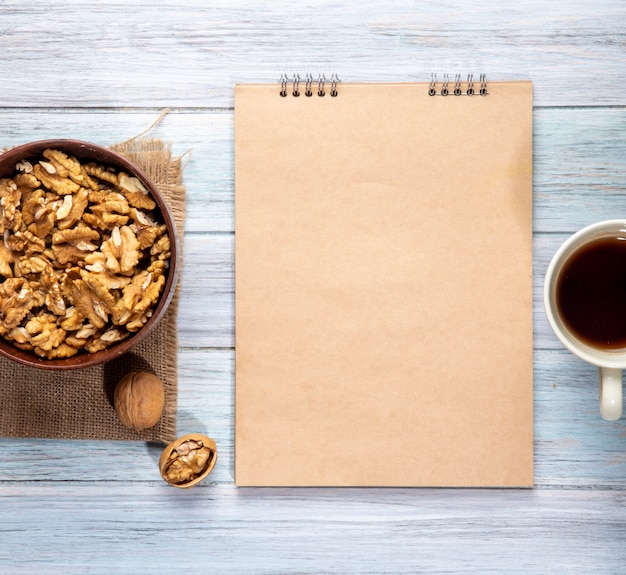 Vista superior de nueces en un tazón cuaderno de bocetos y una taza con té en madera