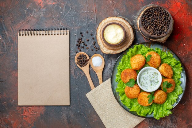 Vista superior de nuggets de pollo lechuga en placa sal y pimienta negra en tazones de madera Bloc de notas en mesa oscura