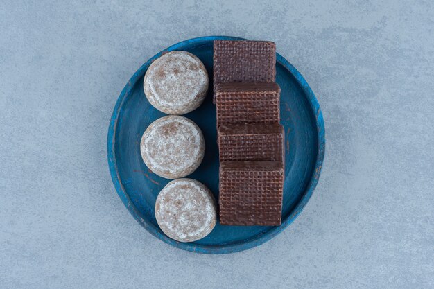 Vista superior de obleas de chocolate con galletas caseras en placa de madera azul.
