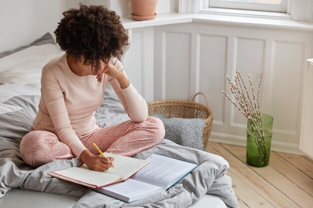 Vista superior de la ocupada mujer de piel oscura escribe registros en el cuaderno del libro