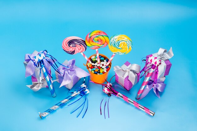 Una vista superior de paletas y regalos alogn con dulces multicolores silbatos de cumpleaños sobre el fondo azul confitura de azúcar dulce caramelo