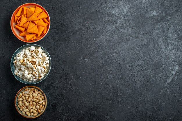 Vista superior de palomitas de maíz frescas con nueces y papas fritas sobre fondo oscuro, papas fritas, bocadillo, galleta crujiente