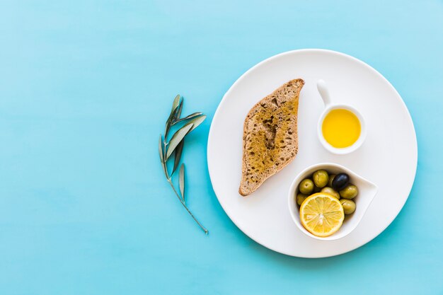 Vista superior de pan con aceitunas y tazón de rodaja de limón sobre el fondo azul