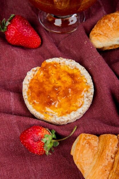 Vista superior de pan crujiente crujiente y fresas con panecillos y mermelada en la superficie de tela bordo