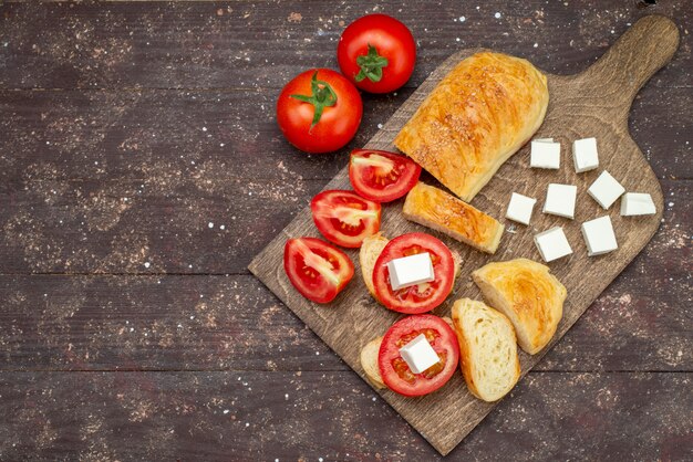 Vista superior pan fresco sabroso bollo largo formado pastelería cortada con queso y tomates en el escritorio de madera marrón bollo masa masa de pan harina