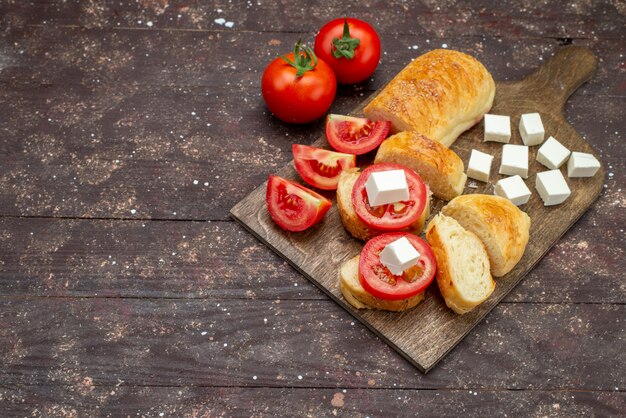 Vista superior pan fresco sabroso bollo largo formado pastelería cortada con queso y tomates en el escritorio de madera marrón bollo masa masa de pan harina