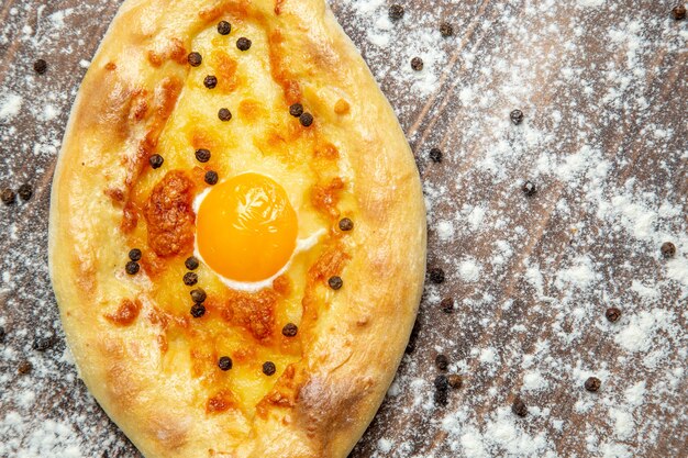 Vista superior de pan horneado con huevo cocido y harina sobre la superficie marrón, masa, huevo, pan, bollo, desayuno