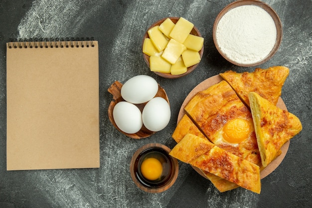 Vista superior de pan de huevo al horno con huevos frescos y queso en rodajas en el espacio gris