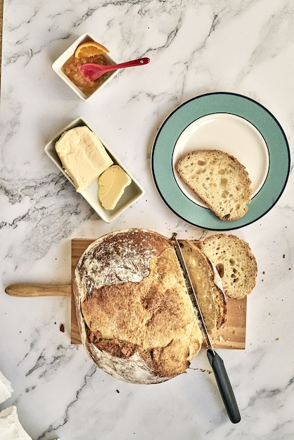 Foto gratuita vista superior de un pan recién horneado en rodajas sobre una tabla de madera con mantequilla y mermelada