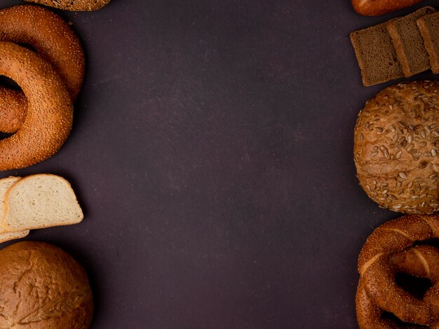 Vista superior de panes como bagel clásico y rebanadas de pan de mazorca de maíz blanco y centeno rebanadas sobre fondo granate con espacio de copia