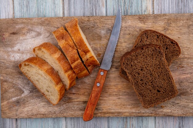 Vista superior de los panes como baguette en rodajas y centeno con un cuchillo en la tabla de cortar sobre fondo de madera