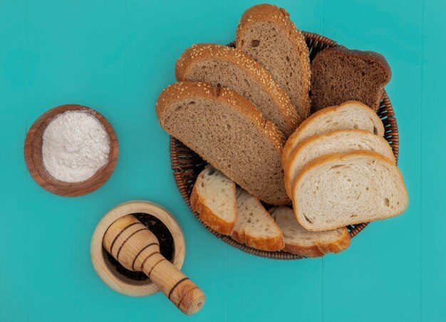 Foto gratuita vista superior de panes como baguette en rodajas sembrado mazorca marrón y centeno en una canasta con harina y pimienta negra sobre fondo azul.