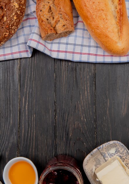 Vista superior de panes como baguettes negras vietnamitas sembradas sobre tela con mantequilla y mermelada en mesa de madera con espacio de copia