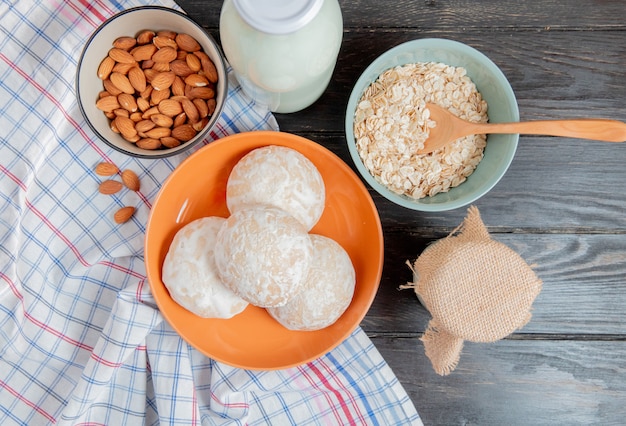 Foto gratuita vista superior de panes de jengibre en plato con almendras sobre tela escocesa y copos de avena de crema de leche agria coagulada con una cuchara en la mesa de madera