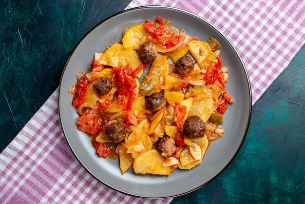 Vista superior de papas al horno con albóndigas y verduras dentro de la placa en el piso azul oscuro.