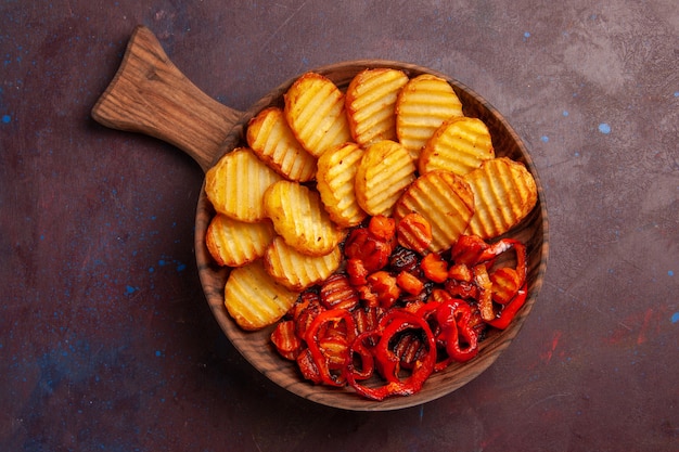 Vista superior de papas al horno con verduras cocidas dentro de la placa en el espacio oscuro