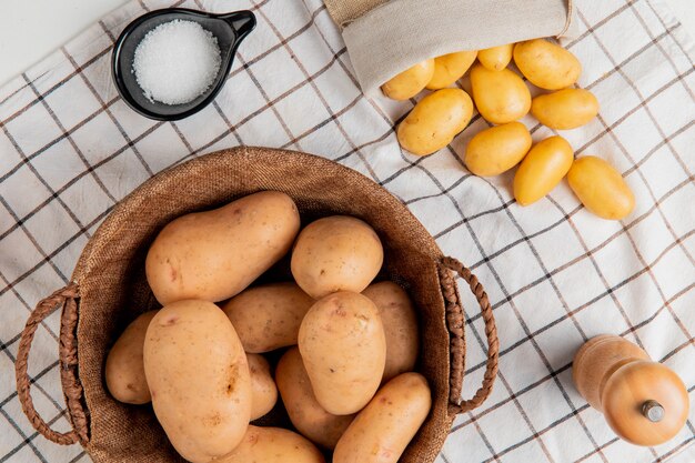 Vista superior de papas en canasta con mantequilla, sal, pimienta negra sobre la superficie del paño