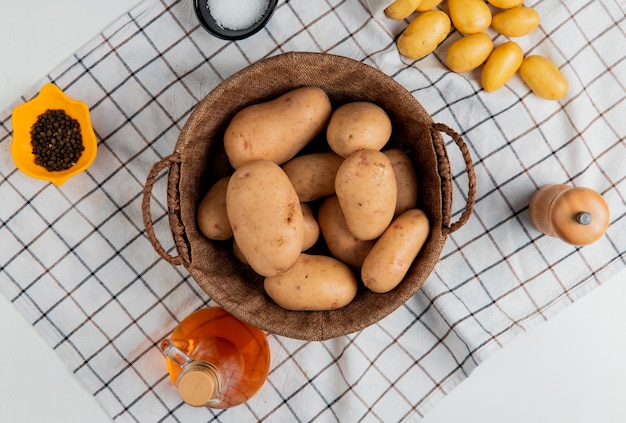 Vista superior de papas en canasta con mantequilla, sal, pimienta negra sobre tela escocesa y superficie blanca