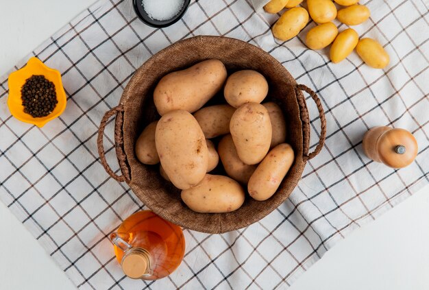 Vista superior de papas en canasta con mantequilla, sal, pimienta negra sobre tela escocesa y superficie blanca