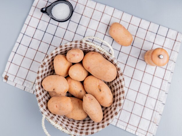 Vista superior de papas en canasta con sal sobre tela escocesa sobre superficie azul