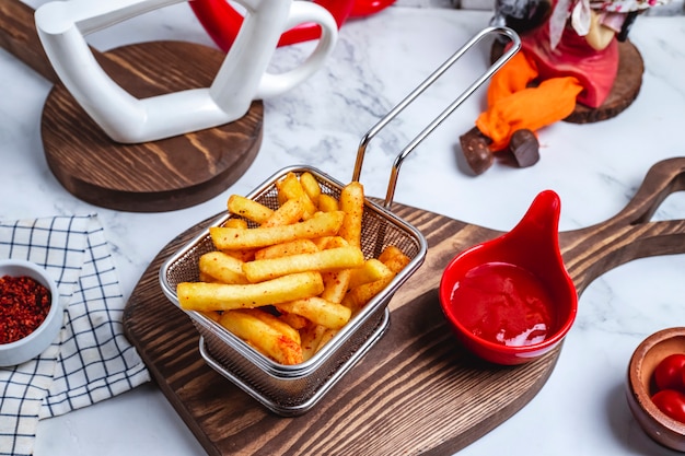 Vista superior de papas fritas en una canasta con salsa de tomate en el tablero