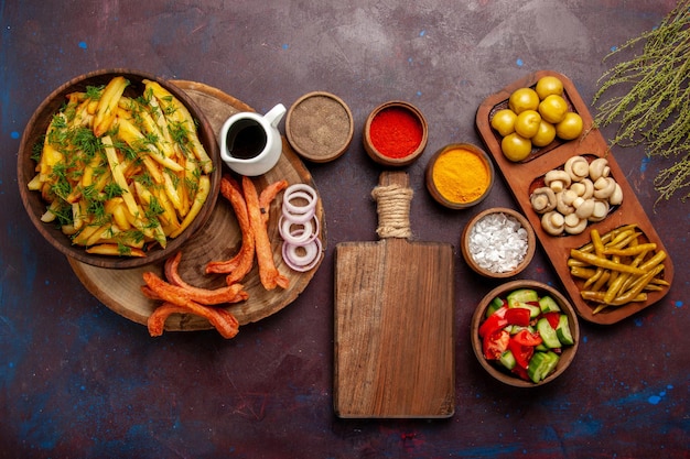 Foto gratuita vista superior de papas fritas con condimentos y diferentes verduras en el escritorio oscuro