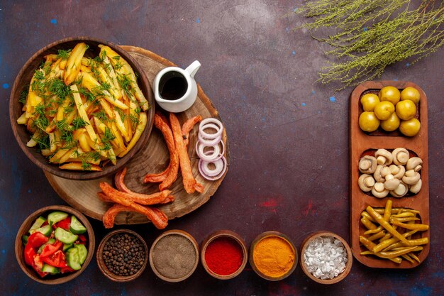 Vista superior de papas fritas con condimentos y diferentes verduras en el escritorio oscuro