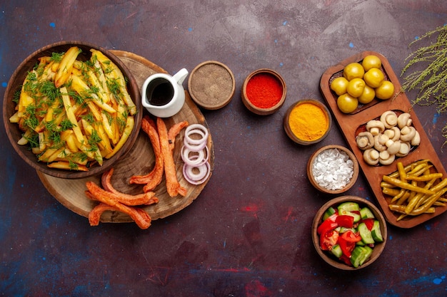 Foto gratuita vista superior de papas fritas con condimentos y diferentes verduras en el escritorio oscuro