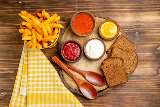 Vista superior de papas fritas con condimentos y panes de pan oscuro en la mesa marrón comida de hamburguesa de pan de patata