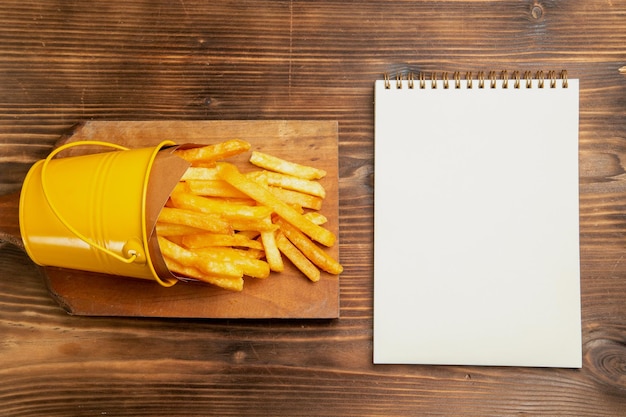 Vista superior de papas fritas dentro de la canasta con el bloc de notas en la mesa marrón