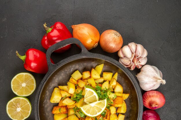 Vista superior de papas fritas dentro de la sartén con diferentes condimentos y verduras en el escritorio oscuro